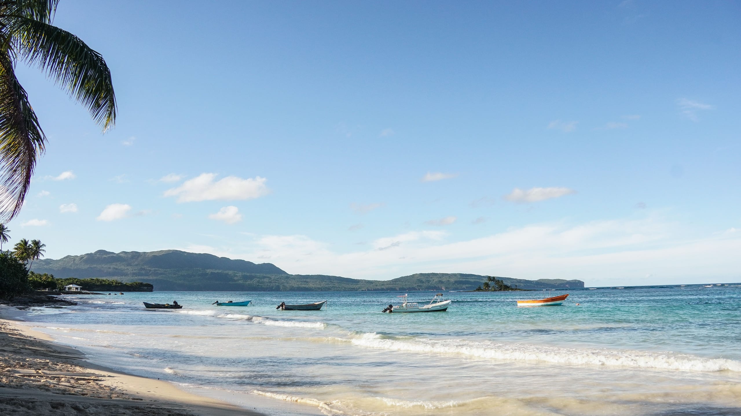 Tropical beach with small boats and palm leaves under a blue sky